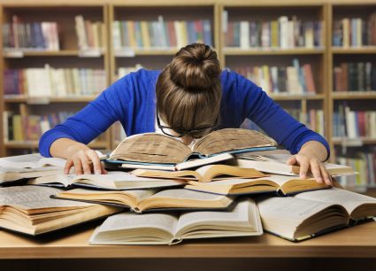 A young female university student slumped over a large pile of books