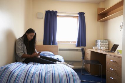 A female student sitting on the bed of her studio apartment