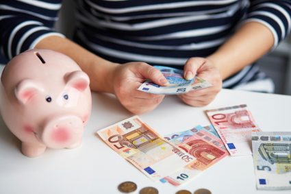 A student counting money with a piggy bank next to him on the table