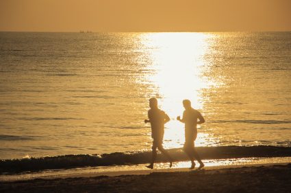 Two people running on a beach at sunset