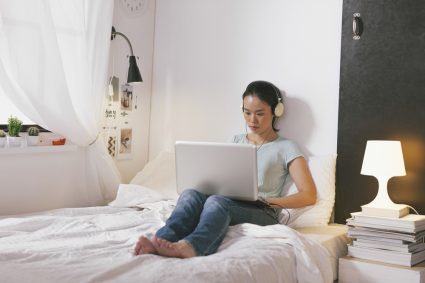 A woman shopping online while sitting on her bed