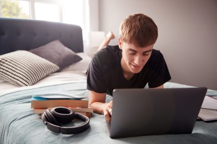 A student working on his laptop in bed