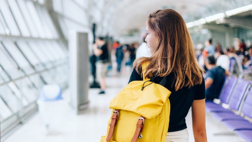 A young traveler in an airport terminal, looking over her shoulder, with a yellow backpack, embarking on an international experience.
