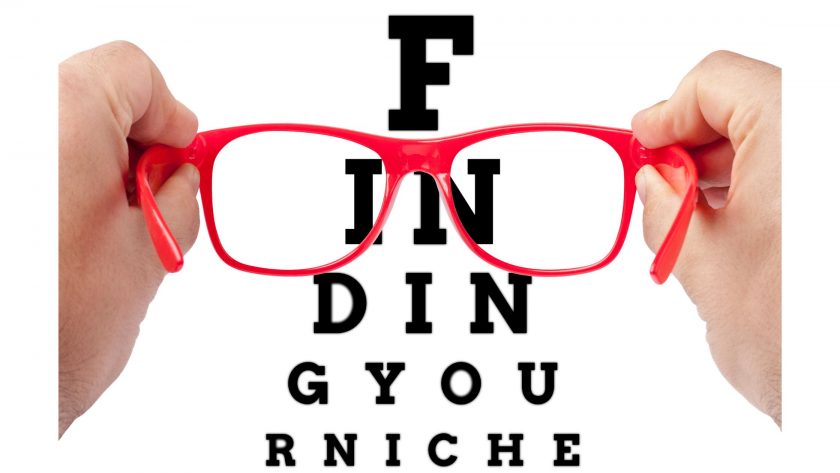 Hands holding red-framed glasses in front of an eye chart that spells 'FINDING YOUR NICHE,' with the letters visible through the glasses.